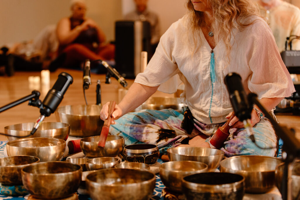 A woman sits on the floor with many gold bowls of varying sizes surrounding her