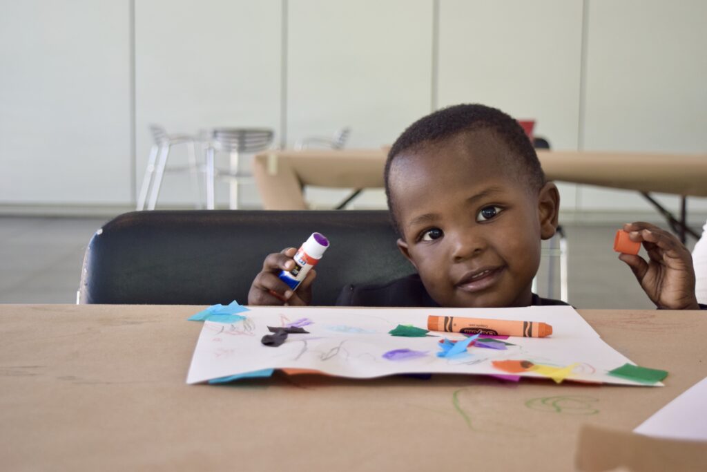 A toddler holds a glue stick and smiles