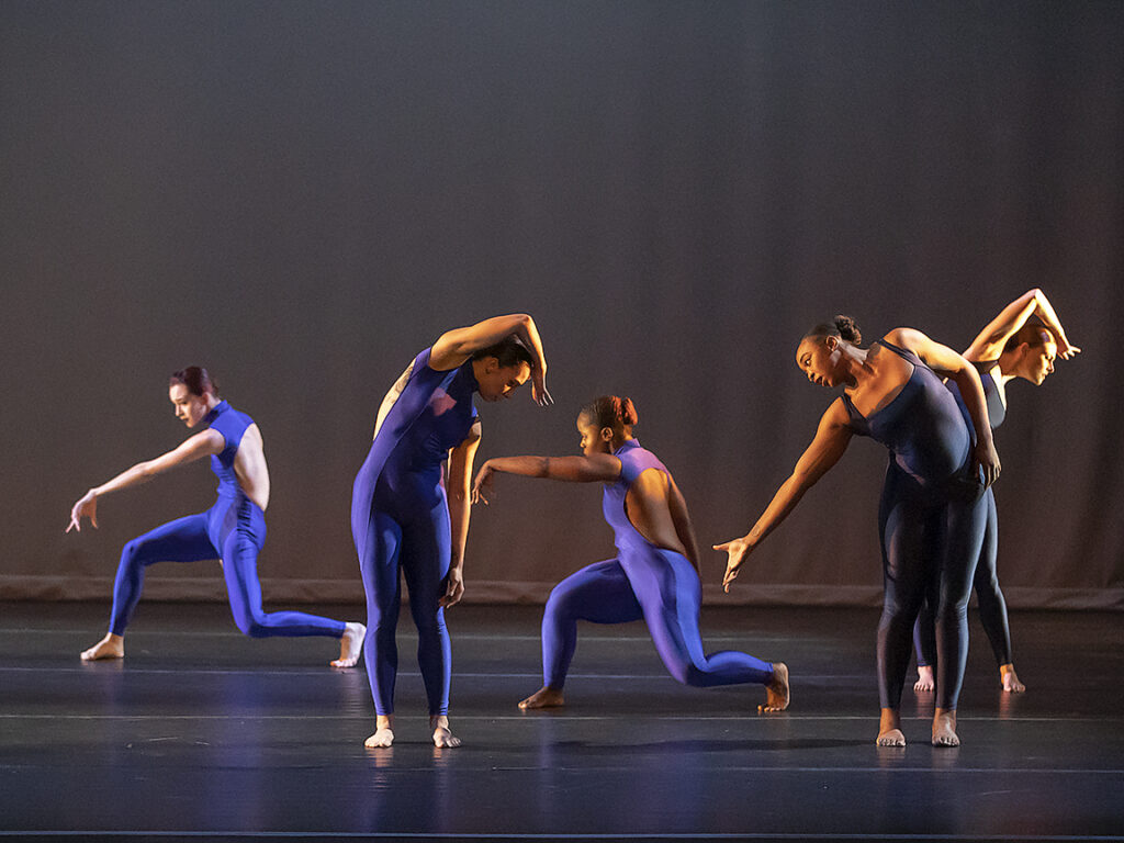 A group of five dancers stand on a stage in varying poses