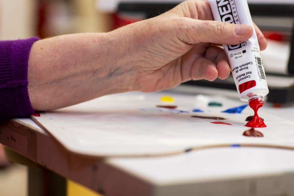 Close up of a hand squeezing red pain our of a bottle onto a paper.