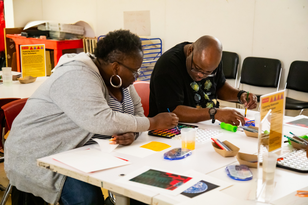 Two individuals water color painting at a table.